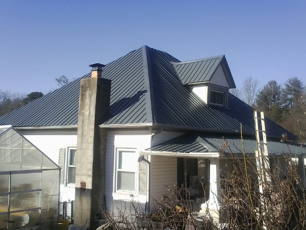 Dark blue standing seam metal roof on a white farmhouse with dormer — Slate & Tile Roof Repair by Roofing Brothers in North Brunswick