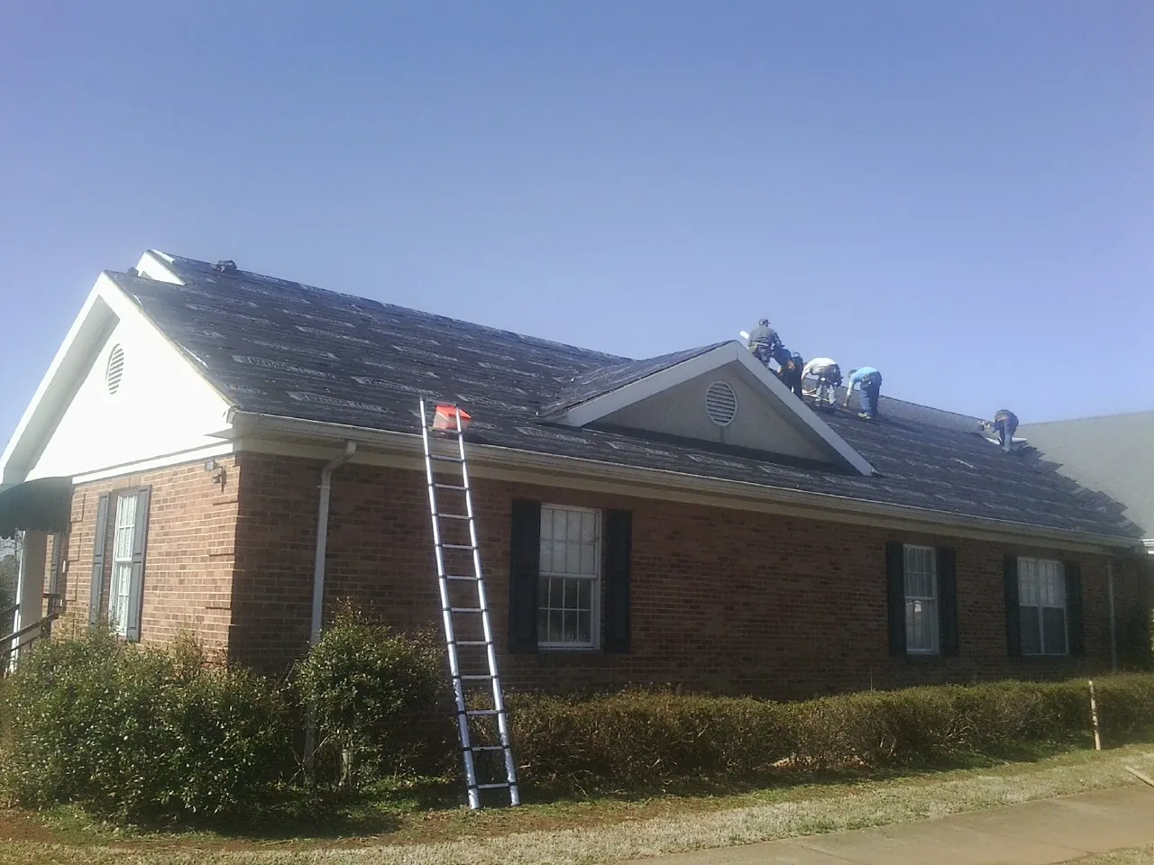Crew tearing shingles off a brick ranch roof with a ladder set — Metal Roof Repair work by our crew in North Brunswick