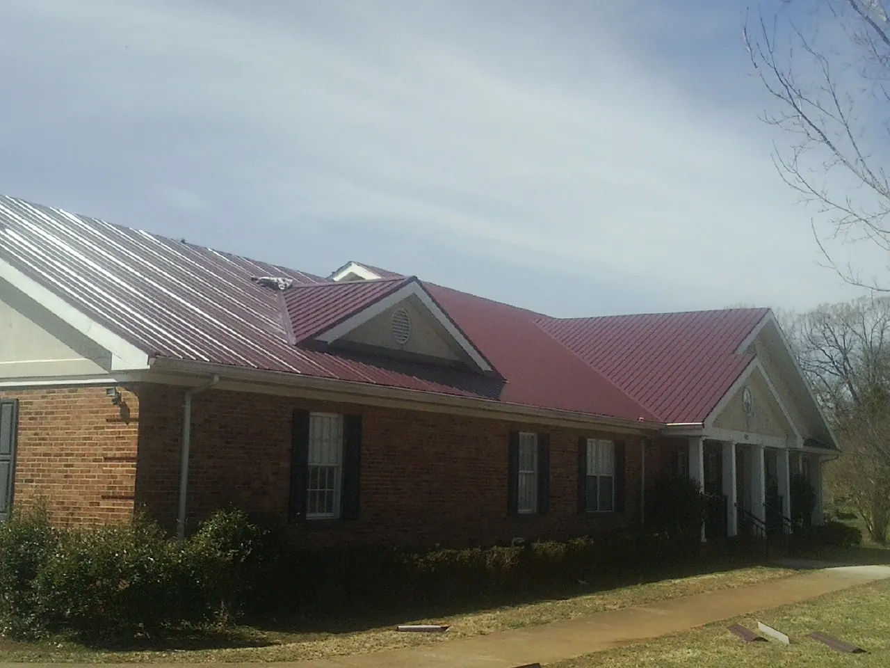 Red metal roof with gabled entries on a long brick building, from a Hail Damage Roof Repair job in North Brunswick