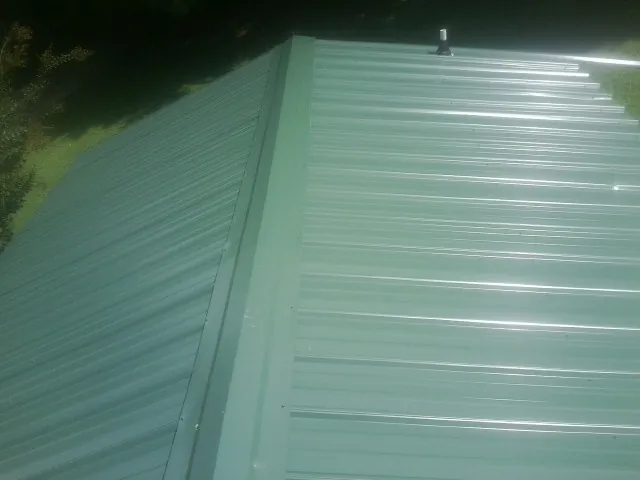 New green metal panels meeting at the ridge of a roof — Flat Roof Repair work by our crew in North Brunswick
