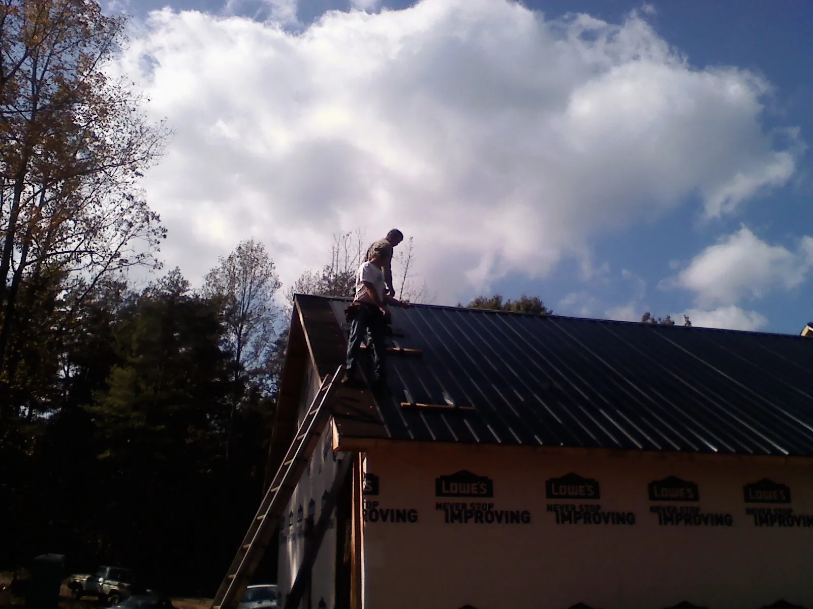 Roofer fastening dark metal panels high against a cloudy sky, from a Roof Inspection job in North Brunswick