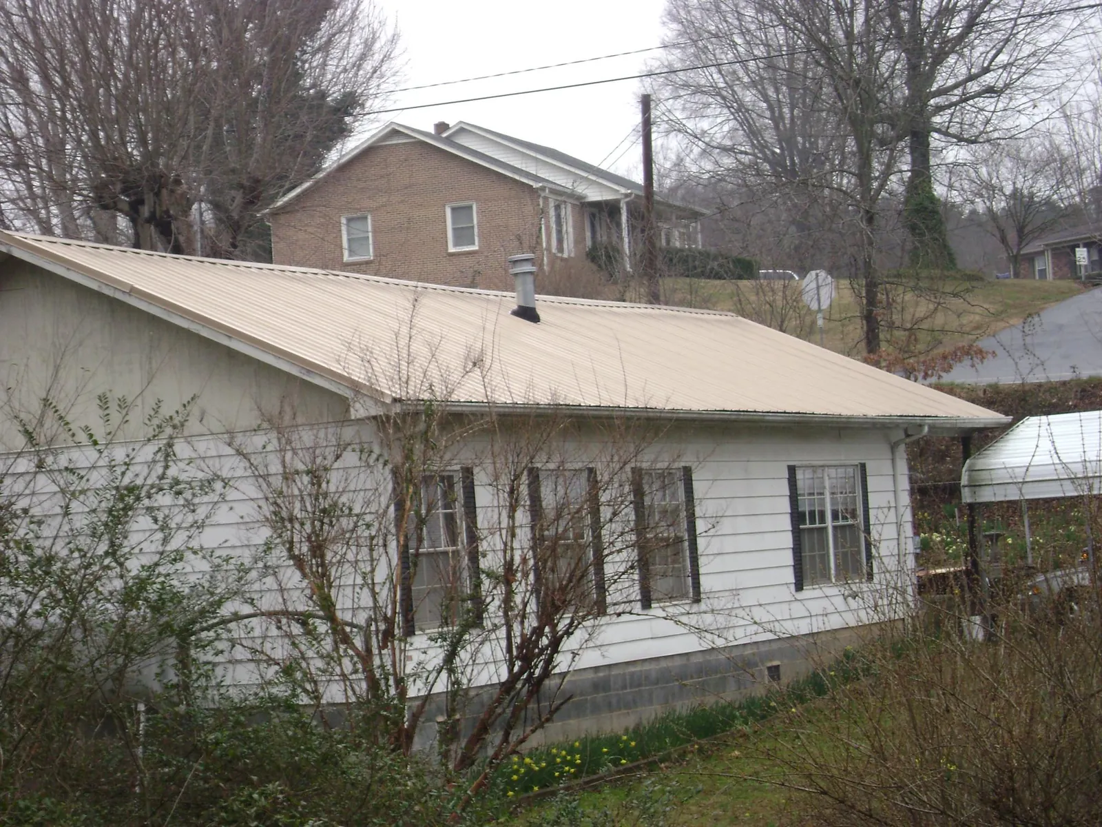 Tan metal roof on a white sided house set into a hillside — Commercial Roofing by Roofing Brothers in North Brunswick
