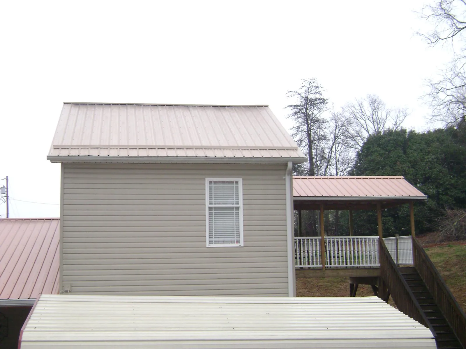 Tan metal roofs on a two story addition and attached porch, from a Roof Replacement job in North Brunswick